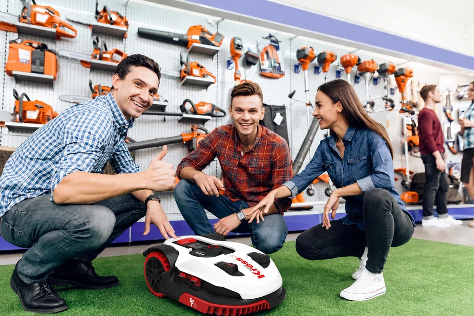 Un mécanicien ou vendeur expert, en tenue professionnelle (polo ou uniforme Thébault Motocultures si possible), présentant ou expliquant le fonctionnement d'un robot de tonte à un client dans un showroom ou atelier. Le mécanicien pointe ou tient une partie de la machine, illustrant son expertise technique et sa connaissance approfondie du produit. L'interaction doit montrer de la confiance et de la compétence, avec l'équipement de tonte visible et en avant-plan.
